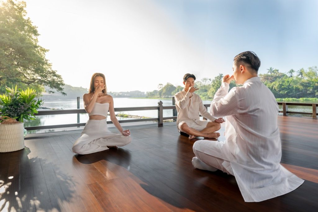 Group practicing mindful breathing meditation by the riverside at RXV Wellness Village Sampran