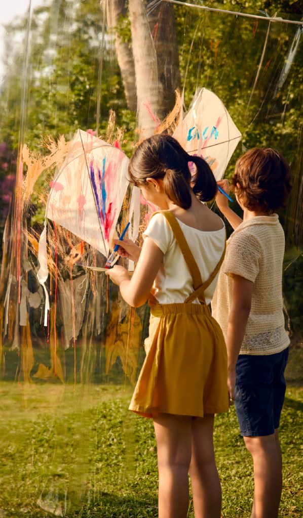 Children painting kites outdoors at RXV Wellness Village, engaging in creative family-friendly wellness activities surrounded by nature.