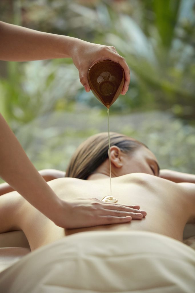 Therapist pouring warm herbal oil on guest’s back during an aromatherapy massage at RXV Wellness Village