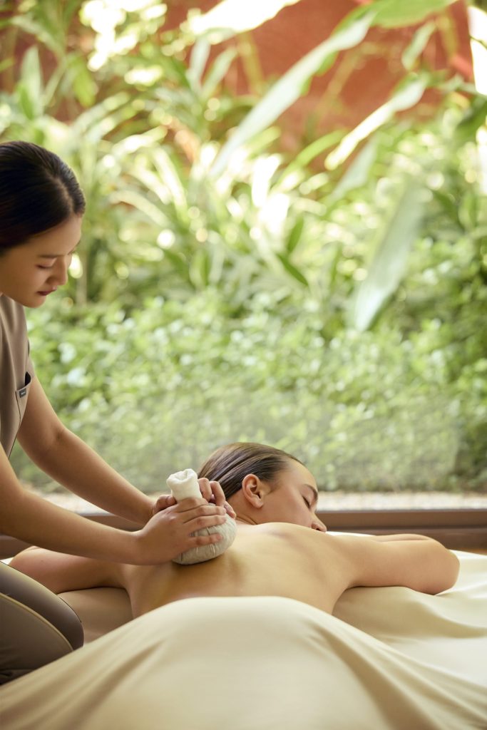 Therapist applying warm herbal compress on guest’s back during a traditional Thai massage at RXV Wellness Village.