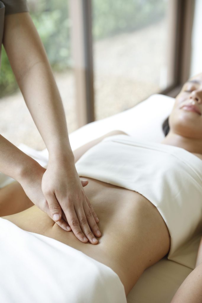 Therapist performing abdominal massage therapy to stimulate gut health and detoxification at RXV Wellness Village.