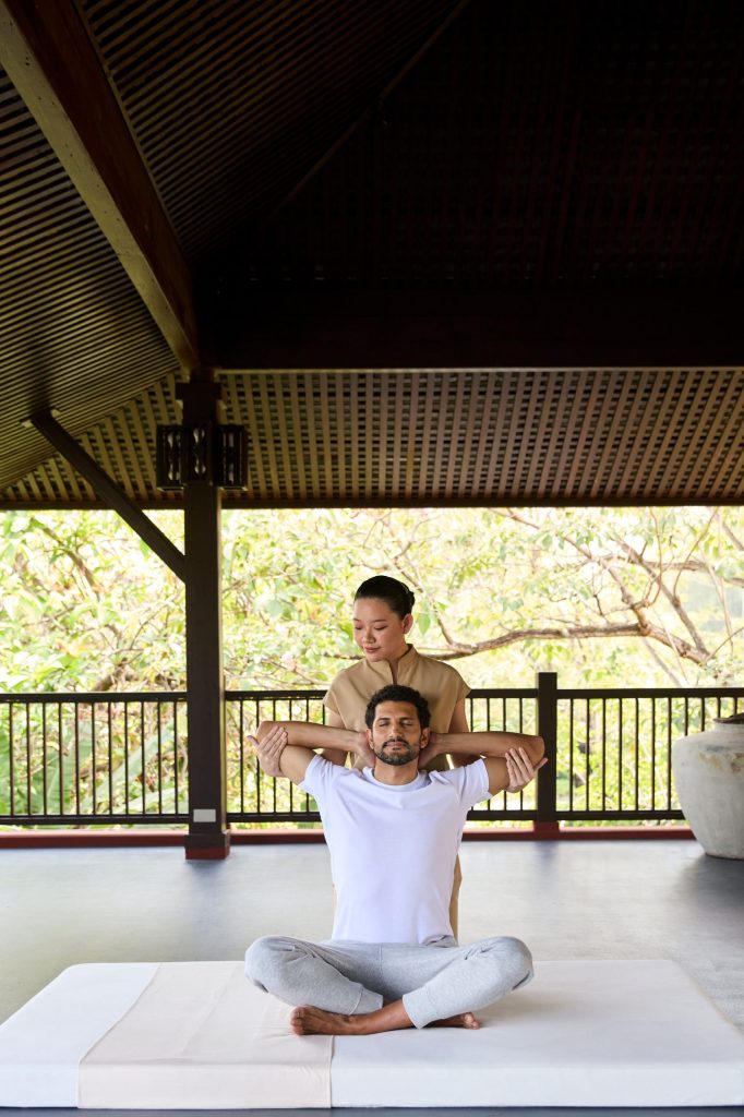 Therapist guiding guest through assisted stretching session on a serene open-air pavilion at RXV Wellness Village.