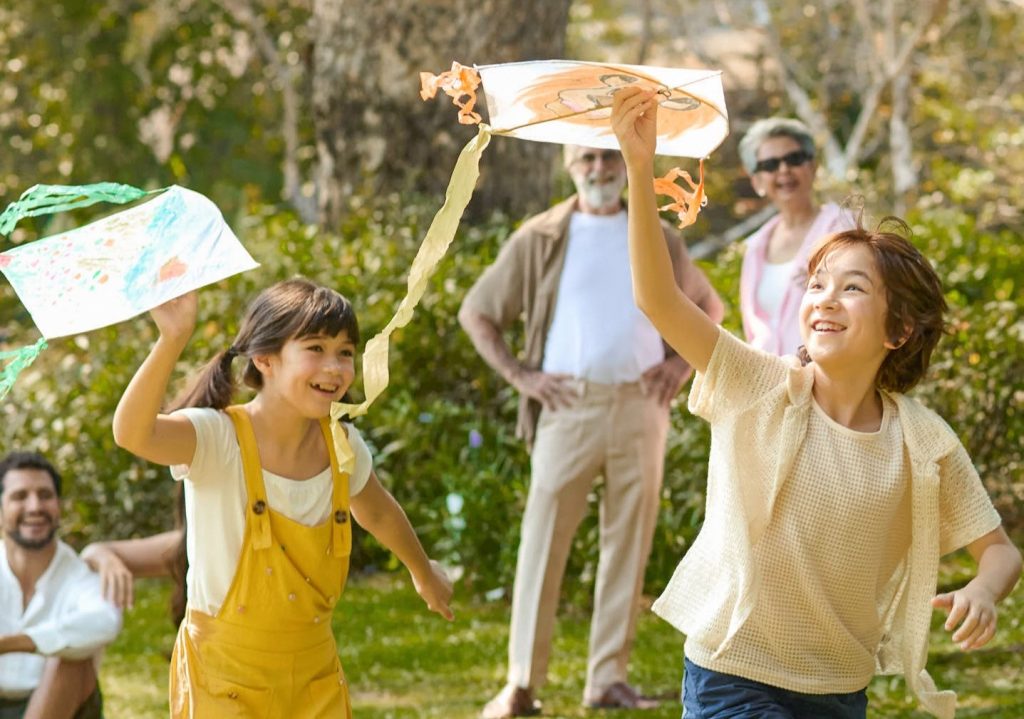 Children joyfully playing with handmade kites outdoors at RXV Wellness Village, surrounded by family — celebrating Thailand’s 2025 family-friendly wellness trends.