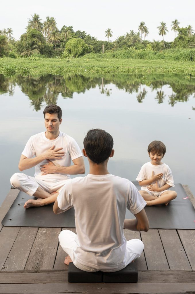Family meditation by the river at RXV Wellness Village, fostering mindfulness and calm in a natural setting.