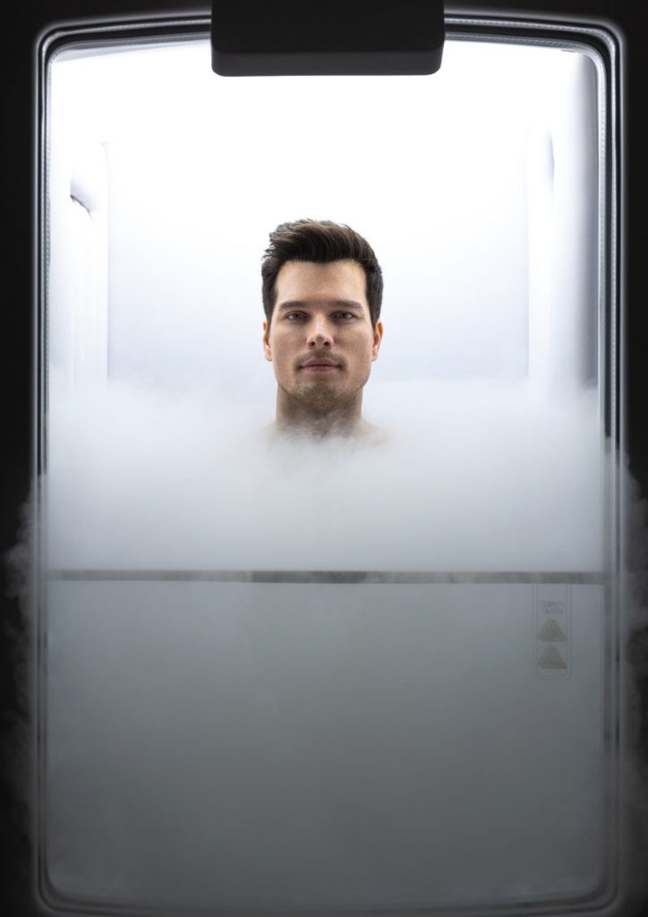 Man experiencing whole-body cryotherapy session surrounded by cooling mist at RXV Wellness Village.