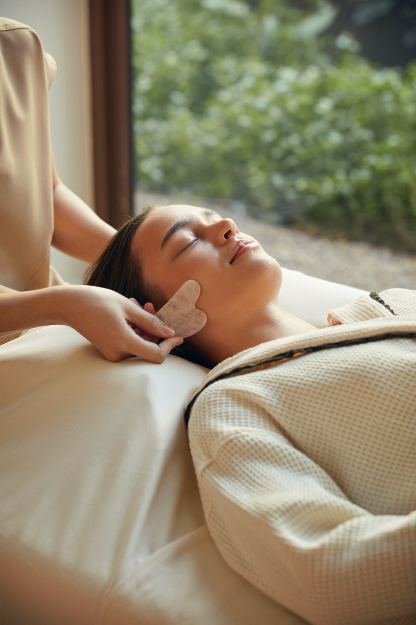 Close-up of a woman receiving a gentle facial massage surrounded by nature at RXV Wellness Village Sampran.