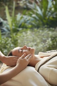 Close-up of a woman receiving a gentle facial massage surrounded by nature at RXV Wellness Village Sampran.