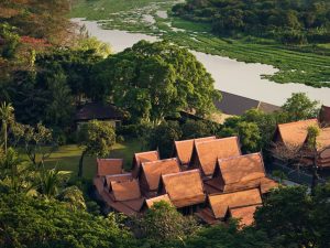 Aerial view of traditional Thai architecture surrounded by greenery and a tranquil river at RXV Wellness Village Sampran.