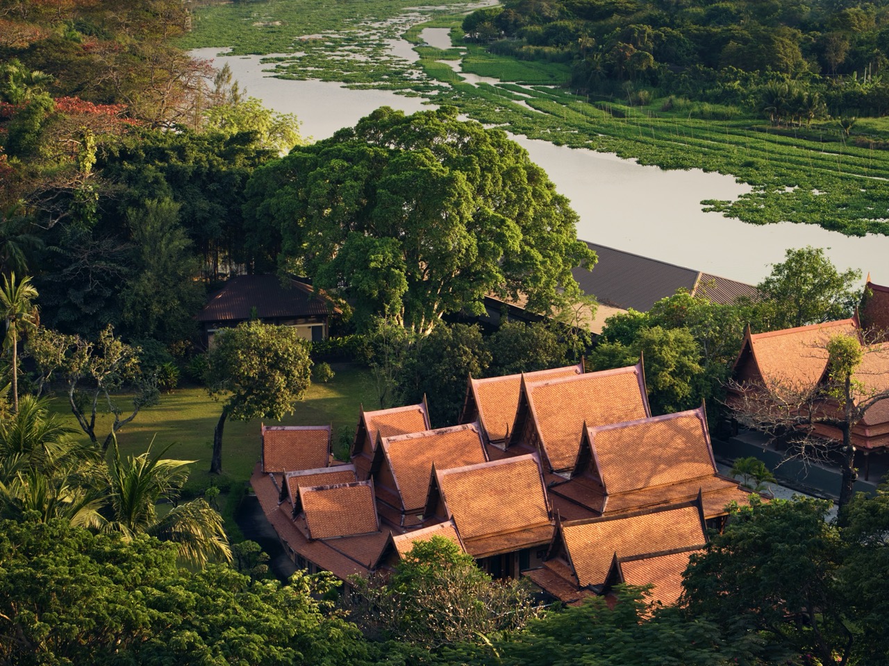 Aerial view of traditional Thai architecture surrounded by greenery and a tranquil river at RXV Wellness Village Sampran.