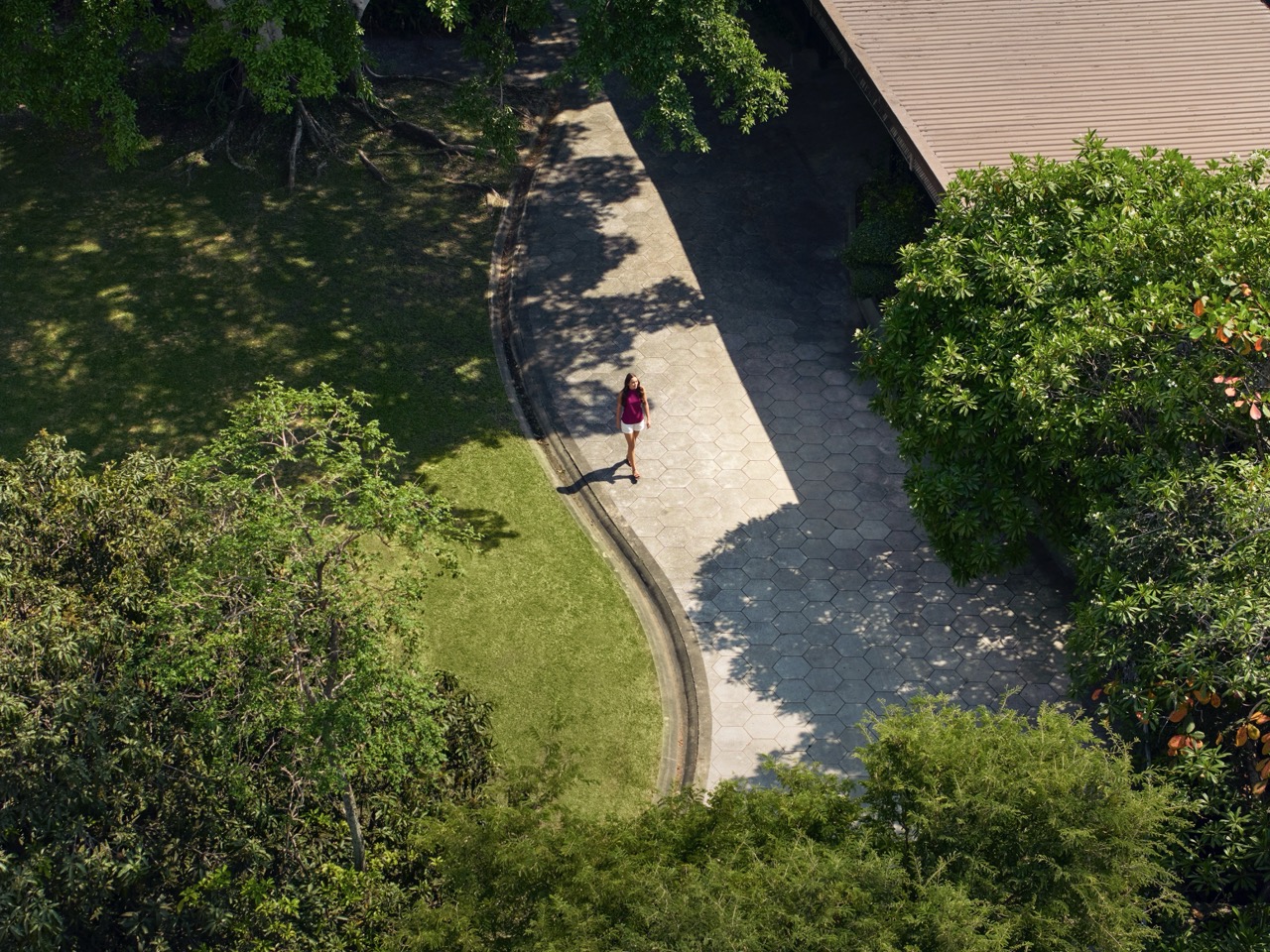 A woman walking alone along a shaded garden path surrounded by lush greenery at RXV Wellness Village Sampran.