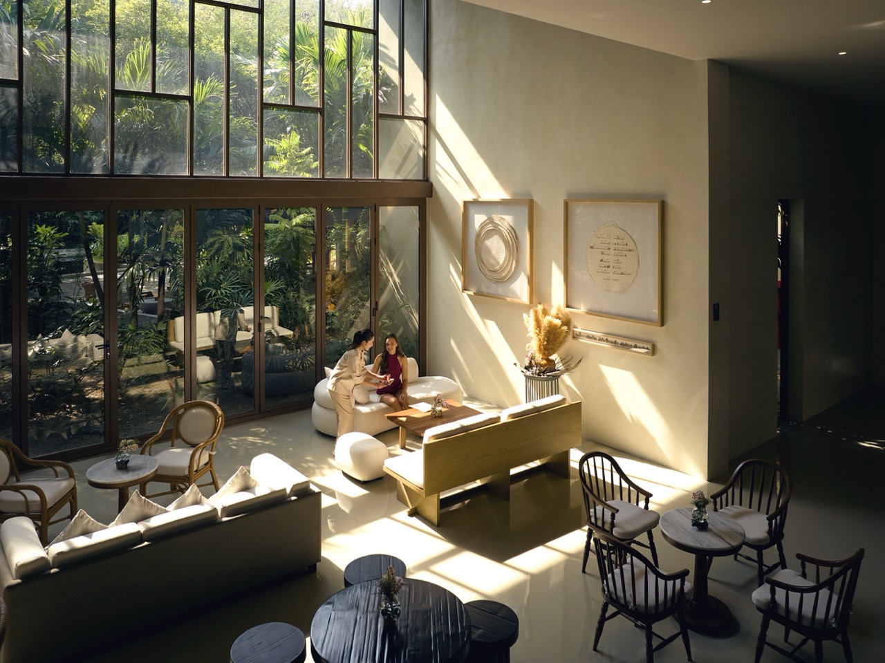 RXV Wellness Village Sampran lobby bathed in natural light, where guests consult with a wellness advisor amidst serene greenery.