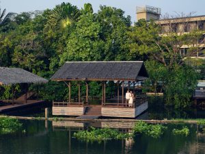 Couple standing on a riverside pavilion surrounded by lush tropical greenery at RXV Wellness Village Sampran.