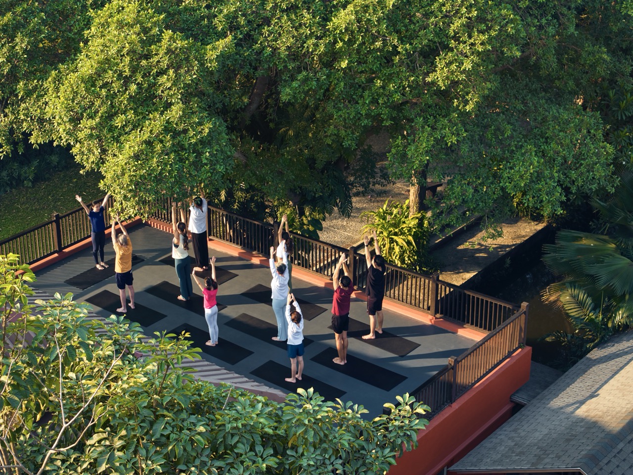 Group rooftop yoga session under the morning sun at RXV Wellness Village Sampran surrounded by lush greenery.