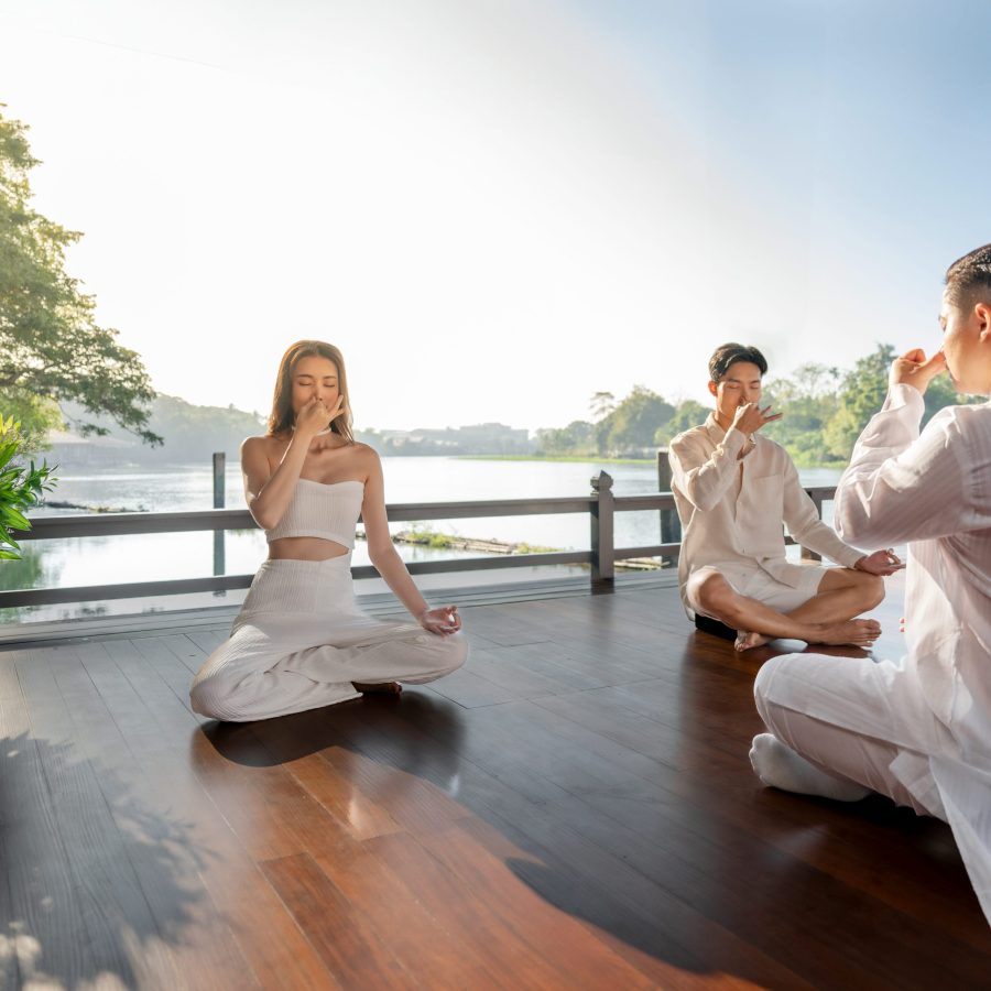 Group practicing mindful breathing meditation by the riverside at RXV Wellness Village Sampran