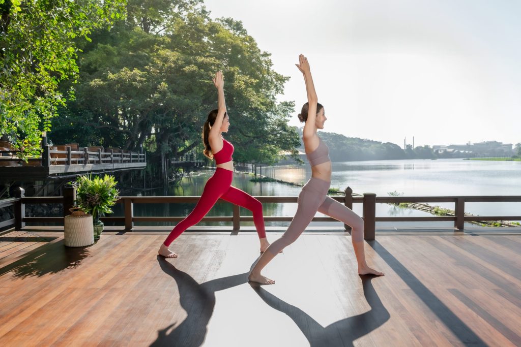 Two women practicing yoga by the riverside deck at RXV Wellness Village Sampran
