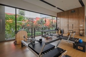 A modern Pilates studio at RXV Wellness Village Sampran featuring reformer machines and wooden interiors with a garden view through large glass windows.