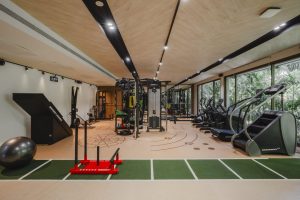 A modern fitness studio at RXV Wellness Village Sampran featuring advanced cardio and strength equipment, functional training zones, and large glass windows overlooking lush greenery.
