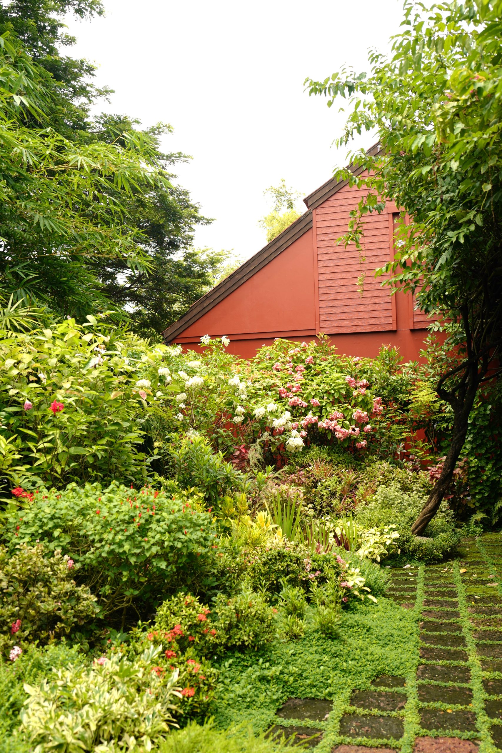 Lush tropical garden with blooming flowers beside a red Thai-style house at RXV Wellness Village Sampran.