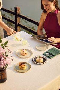 Woman enjoying afternoon tea with wellness desserts by the river at RXV Wellness Village Sampran.