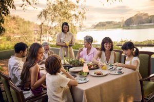 Family enjoying a riverside wellness meal together at RXV Wellness Village Sampran during sunset.