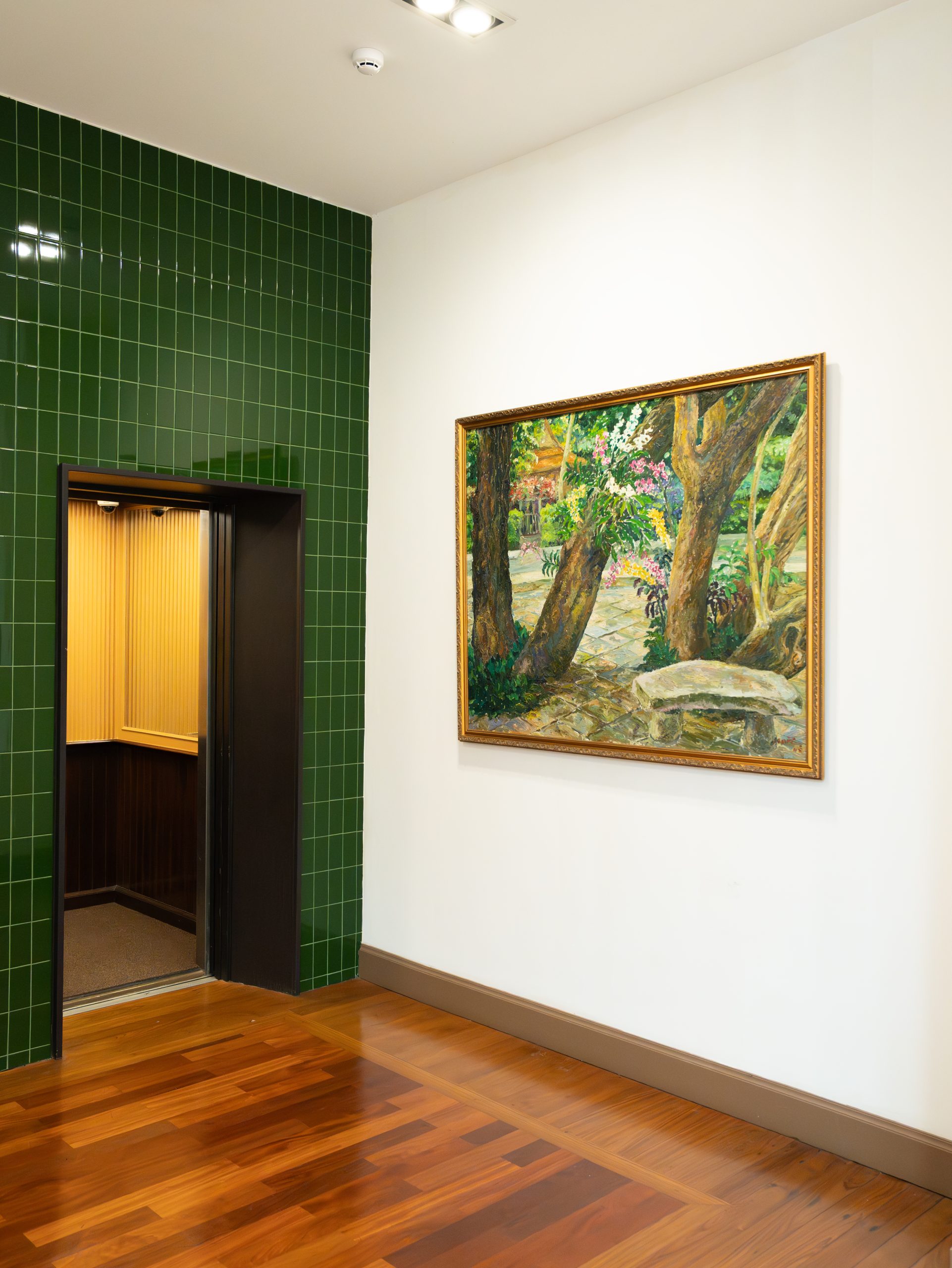 Artistic corner at RXV Wellness Village Sampran featuring a nature painting beside a green-tiled elevator and wooden floor interior.