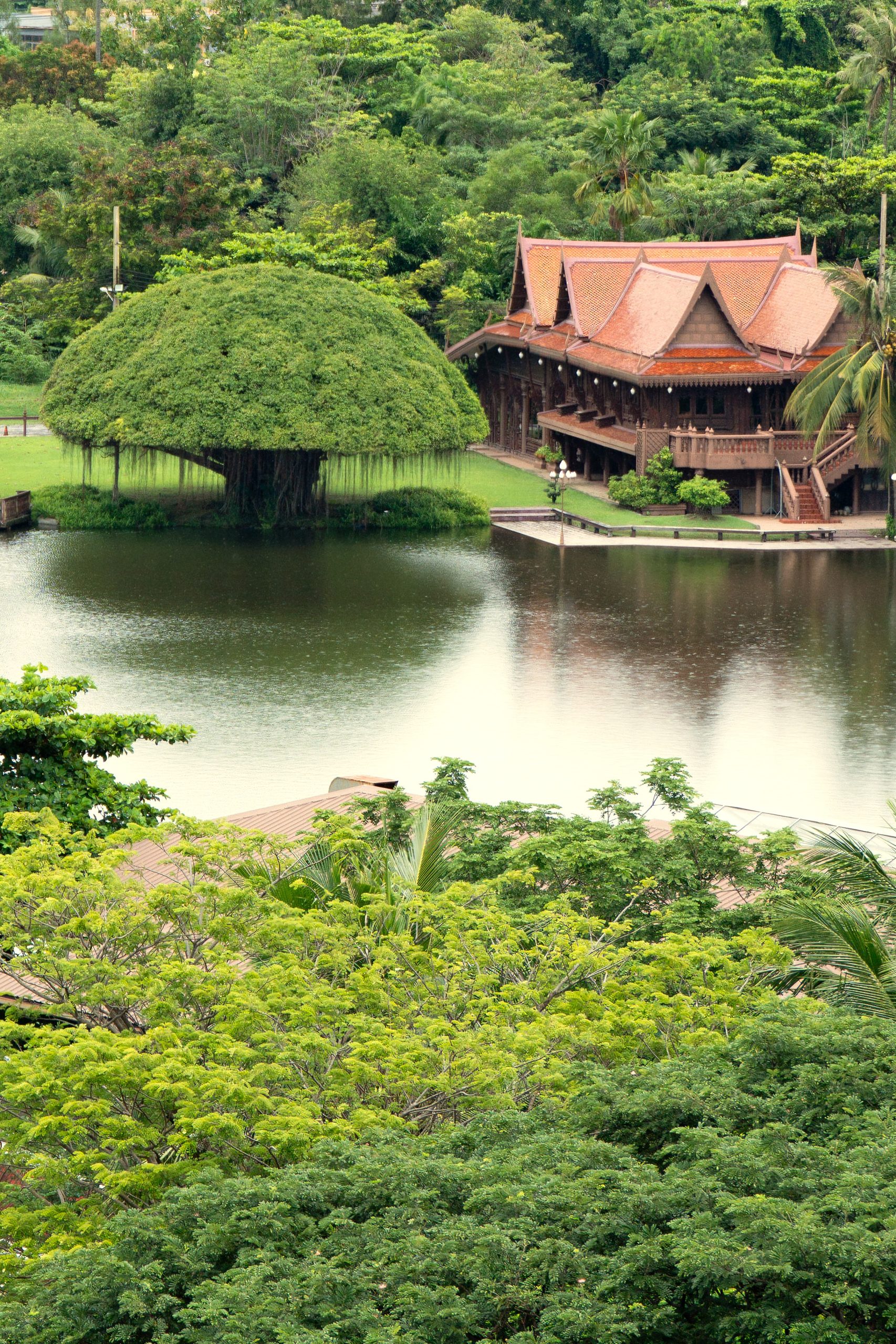 Aerial view of a traditional Thai pavilion beside a serene lake surrounded by lush greenery at RXV Wellness Village Sampran.